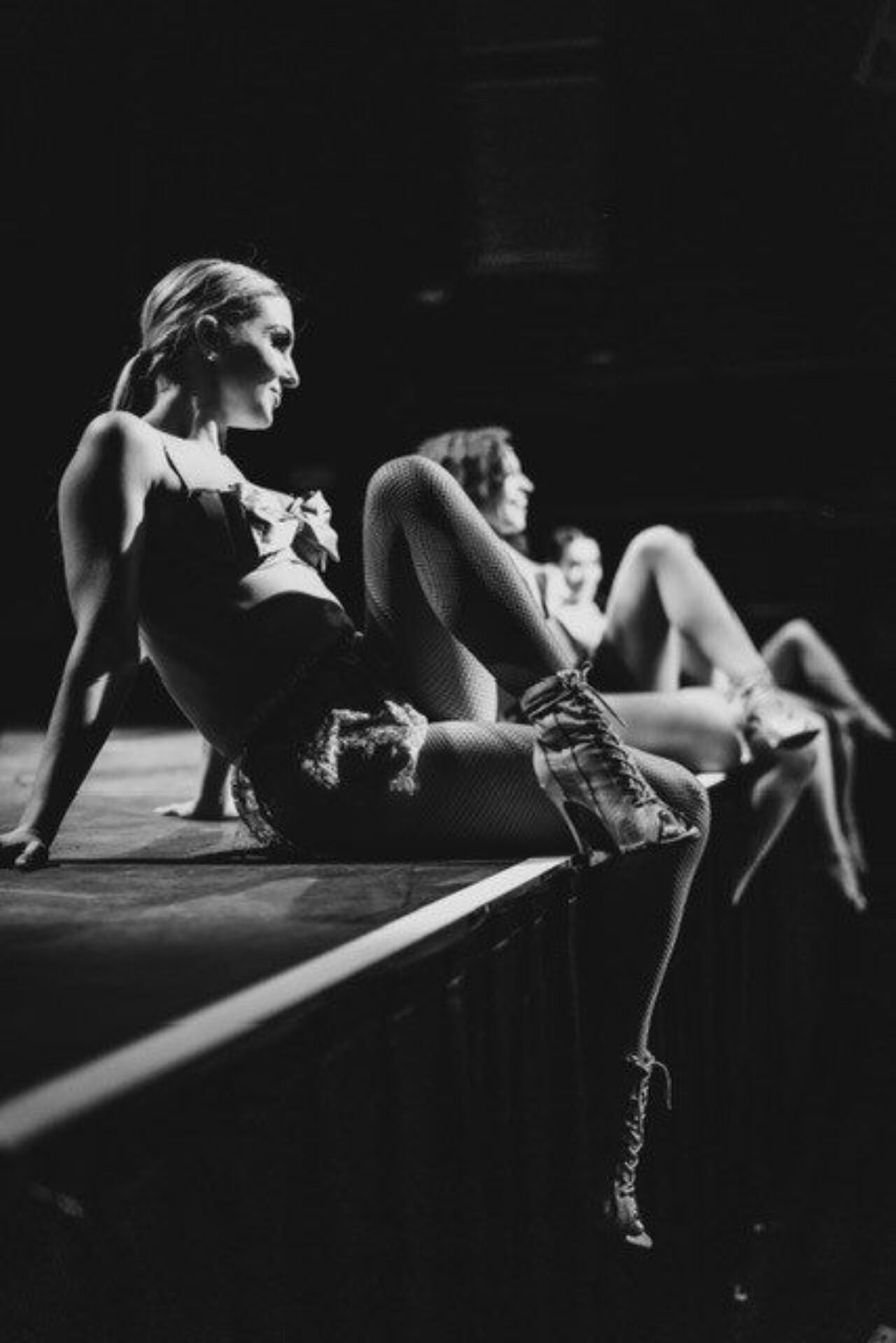 Dancers in fishnets and high heels sitting on the edge of a stage
