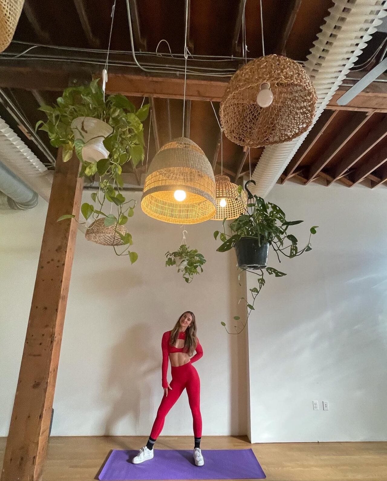 Woman in athletic wear posing under hanging plants and lamps